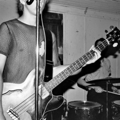 A black and white image of a male guitarist in a mesh shirt.